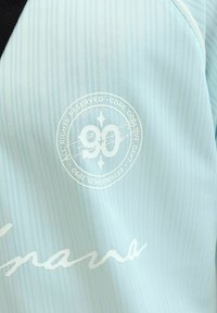 Tissu bleu clair rayé avec un logo circulaire blanc indiquant "90" et un texte incluant "Core Creative Dept" et "Established 1990."