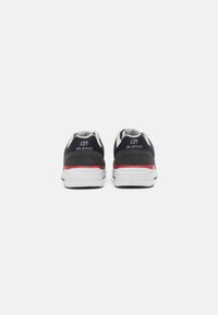 Schwarze und graue Sneakers mit weißen Sohlen, ausgestattet mit einem roten Akzentstreifen, gepolstertem Kragen und einem Logo auf der Ferse. Strukturiertes Material.
