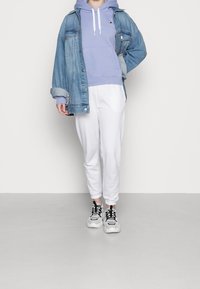 Light blue hoodie with white drawstrings and embroidered logo, layered under a denim jacket, paired with white joggers and black sneakers.