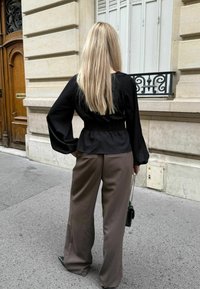 Must-haves mustriga mustaga mustrükkide ja pikade varrukatega musta pluusi ja pruunide laiade pükste kombinatsioon. Aksessuaariks on väike must kott.