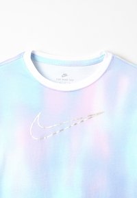 Camiseta de tie-dye en tonos pastel desgastados, con cuello blanco y un logotipo plateado de Nike centrado en el pecho, sobre un fondo liso.