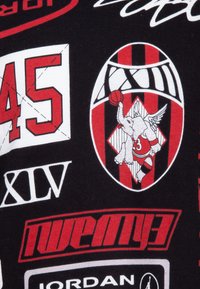 Crna tkanina sa raznim grafičkim zapisima u crvenoj i bijeloj boji, uključujući brojeve, slona s krilima i motiv košarke.