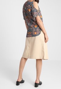 Musteroberteil mit kalten Schultern, ausgestattet mit blauen, orangefarbigen und pinken Blumenmotiven. Khakifarbener A-Linien-Rock und schwarze Blockabsatzschuhe.