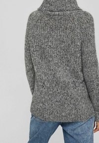 Pull en tricot gris épais avec un col haut, présentant un motif texturé et des épaules légèrement tombantes. L'ourlet est courbé et décontracté.