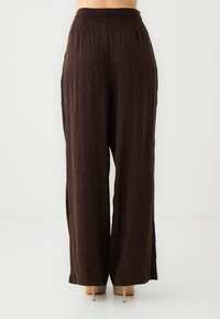 Braune weite Hosen mit texturierter Oberfläche, ausgestattet mit einem elastischen Bund und einem lockeren Schnitt, kombiniert mit beigen High Heels.