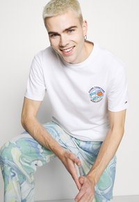 Hvid bomulds t-shirt med et farverigt fredssymbol grafisk design. Lyseblå og grøn marmorering bukser fuldender outfittet.