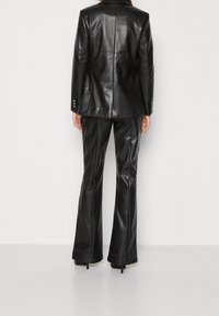 Blazer en cuir noir et pantalon évasé avec une texture lisse. Le blazer est doté d'épaulettes et de boutons en accent. Silhouette ajustée.