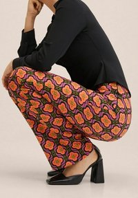 Pantalons évasés avec un motif floral vibrant en rose, orange et vert. Associés à un haut ajusté noir et des chaussures à talons hauts noires.