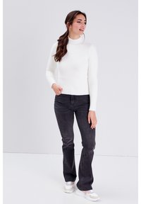 Un pull col roulé blanc côtelé, au design ajusté avec des manches longues, associé à un jean évasé gris foncé et à des baskets blanches décontractées.