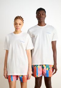 Witte katoenen t-shirts met korte mouwen, met een blauw logo op de borst. Kleurrijke zwemshorts met een bloemen- en streepdessin.