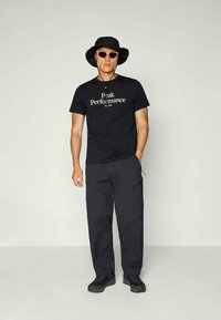 Zwarte katoenen t-shirt met witte print, gecombineerd met donkere cargobroeken. Accessoires zijn een zwarte bucket hat en zonnebril. Schoeisel is zwart.