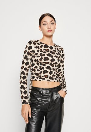 Pöttyös, bézs és fekete színű, hosszúujjú crop top, fényes fekete bőrnadrággal párosítva. Sima textúra és passzos fazon.