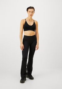 Sujetador deportivo negro con tirantes finos, combinado con leggings de campana negros de cintura alta; ambos hechos de tela elástica, adecuados para ropa deportiva.