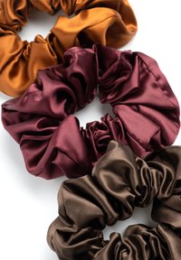 Drie satijnen scrunchies in gebrand oranje, bordeauxrood en donkerbruin, met een gerimpeld ontwerp en een gladde textuur.