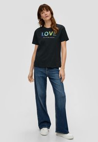 Zwarte katoenen T-shirt met multikleuren pailletten tekst "LOVE" met daaronder een script. Gecombineerd met brede blauwe jeans en witte sneakers.