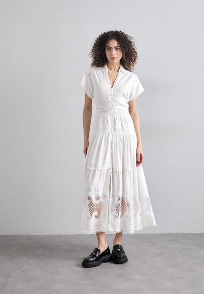 Vestido blanco de botón con mangas cortas, diseño de volantes y detalles de encaje en el dobladillo. Combinado con mocasines negros de plataforma.