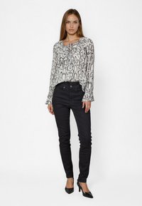 Blouse à manches longues avec un imprimé serpent noir et blanc, dotée d'un col rond et de poignets à volants, assortie à un jean skinny noir et des talons.