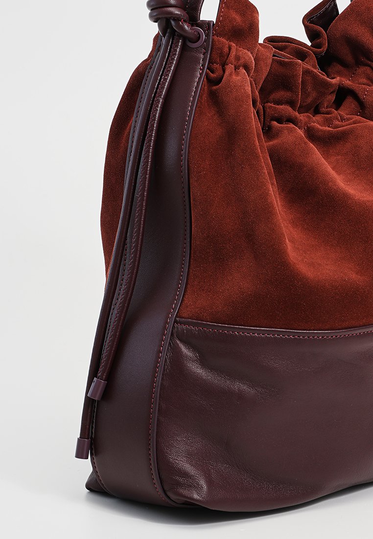 Torebka z zamszu i skóry w głębokim burgundowym kolorze, z zaciśniętym topem i gładką teksturą z widocznymi detalami szycia.
