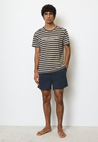 Randig kortärmad skjorta i beige och marin, med en logotyp; parat med marinblå shorts. Enkelt, avslappnat design, bomullsmix.