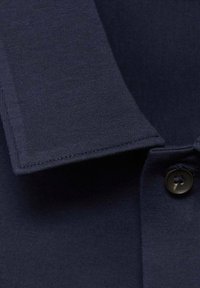 Navy katoenen polo shirt met een gestructureerde kraag, knoopdetails en een gladde textuur. Focus op de kenmerken van de kraag en knopen.