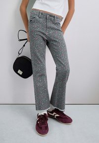 Pantalones grises con un corazón rosa y un patrón de leopardo, diseño de pierna recta, combinados con zapatillas burdeos. Pequeño bolso negro en el hombro.