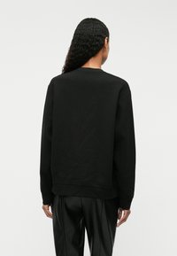 Μαύρη βαμβακερή μπλούζα με στρογγυλή λαιμόκοψη, ριμπ μανίκια και τελείωμα. Λείο ύφασμα με χαλαρή εφαρμογή, φαίνεται από πίσω.