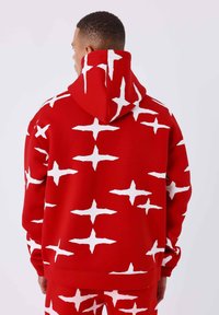 Sudadera roja con un gran estampado de estrella blanca, con un bolsillo tipo canguro y capucha con cordón. Tejido suave con un corte relajado.
