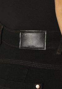Jeans in denim nero con un'etichetta in pelle testurizzata in vita con testo impresso. Dettaglio di cucitura a contrasto lungo le cuciture.