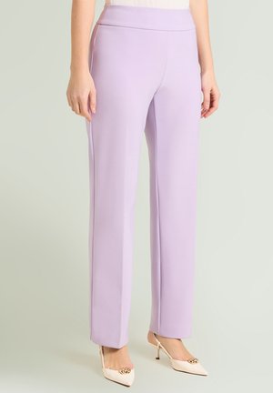 Kvinde iført højtaljede, rette lavendelbukser kombineret med hvide spidse hæle med guldkæde-detalje.