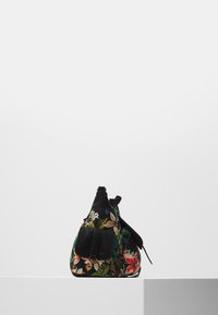 Czarna torebka z kolorowym kwiatowym wzorem, przednią kieszenią z klamrą i regulowanym paskiem, umieszczona na białej platformie na jednolitym tle.