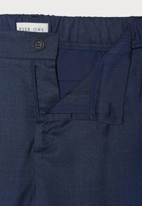 Pantalon bleu marine en tissu texturé, avec fermeture à bouton et taille élastique, doté d'une poche cachée.