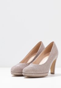 Błyszczące jasnobrązowe szpilki z okrągłym czubkiem, gładką powierzchnią i masywnym obcasem. Platforma zwiększa stabilność.