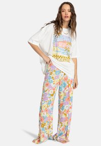 Overdimensioneret hvid t-shirt med farverigt grafisk tryk, kombineret med lette, blomsterede, vide bukser i pastelfarver.