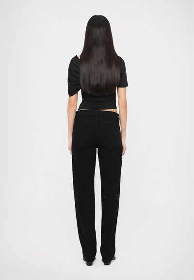 Čierny priliehavý top a voľné čierne nohavice. Hladká látka s jemným leskom. Pohľad zozadu zobrazuje dlhé rovné vlasy a minimalistický štýl.