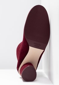 Bota de tobillo de ante burdeos con punta redondeada, tacón bajo de bloque y suela de goma texturizada. Líneas limpias y acabado suave.