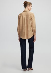 Beige striped shirt with long sleeves, back pleats, and a collar, paired with dark blue jeans and beige high-heeled sandals.