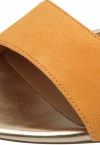 Orange mockasinsandal med en bred rem, mjuk textur och en metallisk guldaccent på sulan. Närbild som framhäver sömnadsdetaljer.