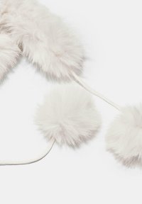 Kolme valkoista pörröistä pom-pomia, jotka on kiinnitetty ohuilla valkoisilla naruilla vaalealla taustalla.