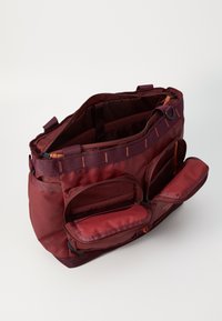 Bordeauxkleurige tas van duurzame stof met meerdere vakken, ritsen en oranje accenten; gestructureerde vorm en zachte binnenvoering.