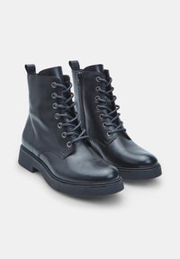 Un paio di stivali neri in pelle fino alla caviglia con punte rotonde, lacci frontali, zip laterali e suole spesse in gomma su sfondo bianco.