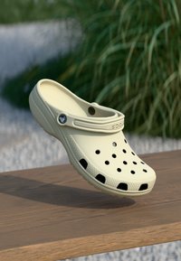 Sabot beige léger en matériau synthétique, doté de trous de ventilation, d'une sangle arrière et d'une semelle texturée pour une meilleure adhérence.
