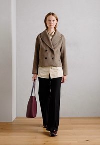 Brown double-breasted wool jacket, cream shirt, black wide-leg trousers, and burgundy tote bag, with glossy brown shoes. Plain background.
