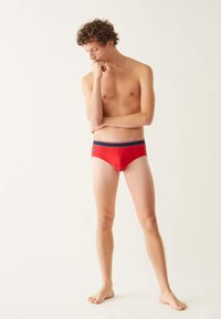 Slips de bain pour hommes rouges avec une taille en tissu bleu marine et des rayures blanches. Le tissu semble lisse et extensible, avec un logo sur le côté.