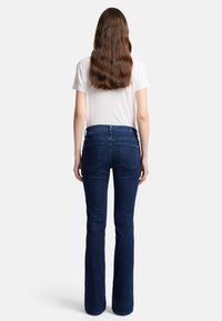Donkerblauwe flare jeans met een soepele textuur, hoge taille en klassiek vijf-pocket design, gecombineerd met een fitted wit T-shirt.