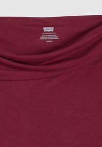 Μπουρντό, μαλακό βαμβακερό πουκάμισο με ντραπαρισμένο λαιμόκοψη. Οι πληροφορίες φροντίδας περιλαμβάνουν την επ ωνυμία "Levi's" και πληροφορίες υφάσματος που βρίσκονται στον γιακά.