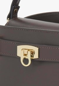 Gros plan sur un sac à main en cuir marron foncé montrant les bords cousus et un fermoir en métal doré avec un mécanisme de verrouillage circulaire.