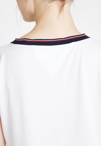 Biała koszulka z granatowym kołnierzykiem w czerwono-białe paski. Projekt obejmuje okrągły dekolt i krótkie rękawy.