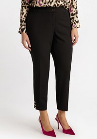 Pantaloni neri su misura con una vestibilità slim e dettagli con bottoni dorati all'orlo. Indossati con tacchi a spillo rosa brillante. Tessuto texturizzato.