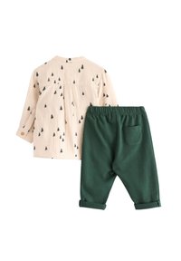 Beige overhemd met lange mouwen met zwarte boomprints, gecombineerd met donkergroene broek met elastische tailleband, voorzien van een achterzak en omgeslagen mouwen.