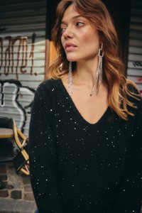 Juodas megztas megztinis su V formos iškirpte, papuoštas išmėtytais sidabriniais blizgučiais. Ilgi, žėrintys auskarai papildo įvaizdį, fone matomas grafičio piešinys.